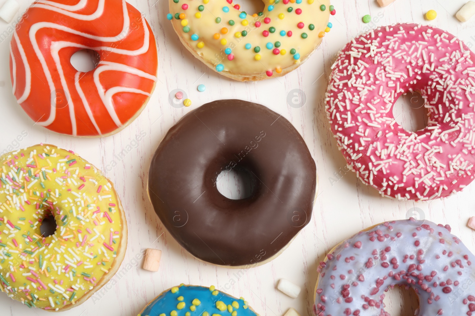 Photo of Delicious glazed donuts on white wooden table, flat lay