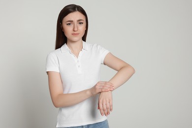 Photo of Young woman suffering from pain in her hand on light grey background, space for text. Arthritis symptoms