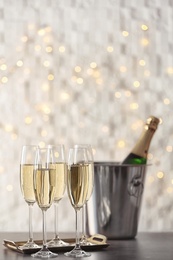 Glasses with champagne and bottle in bucket on table against blurred lights