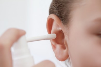 Mother spraying medication into daughter's ear on light background, closeup