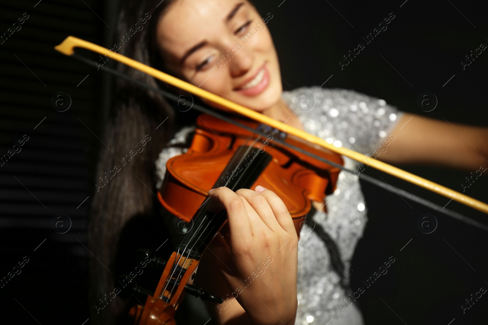 Photo of Beautiful young woman playing violin in dark room, closeup