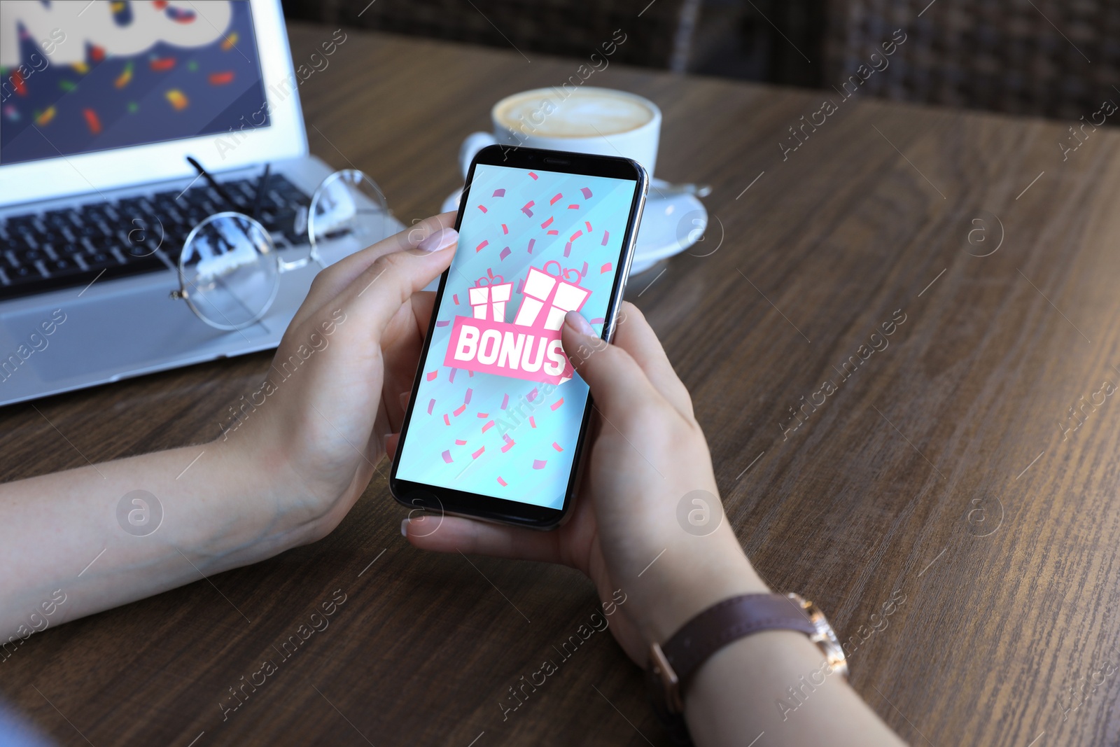 Image of Bonus gaining. Woman using smartphone at wooden table, closeup. Illustration of open gift boxes, word and falling confetti on device screen