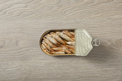 Photo of Open tin can of sprats on wooden background, top view