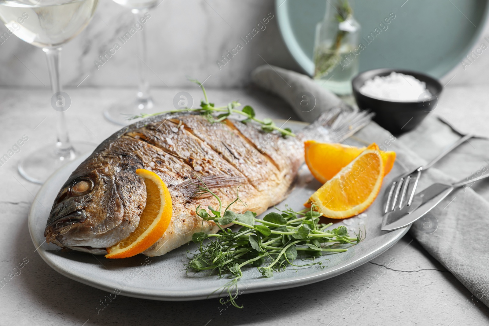 Photo of Seafood. Delicious baked fish served with orange and microgreens on light textured table, closeup