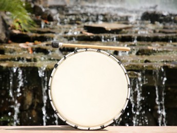 Photo of Drum with mallet near waterfall outdoors on sunny day. Percussion musical instrument