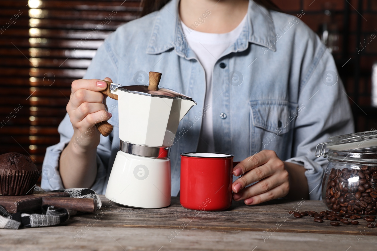 Photo of Brewing coffee. Woman with moka pot, cup and muffin at wooden table, closeup