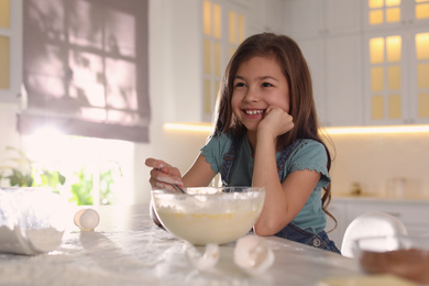 Cute little girl cooking dough in kitchen at home