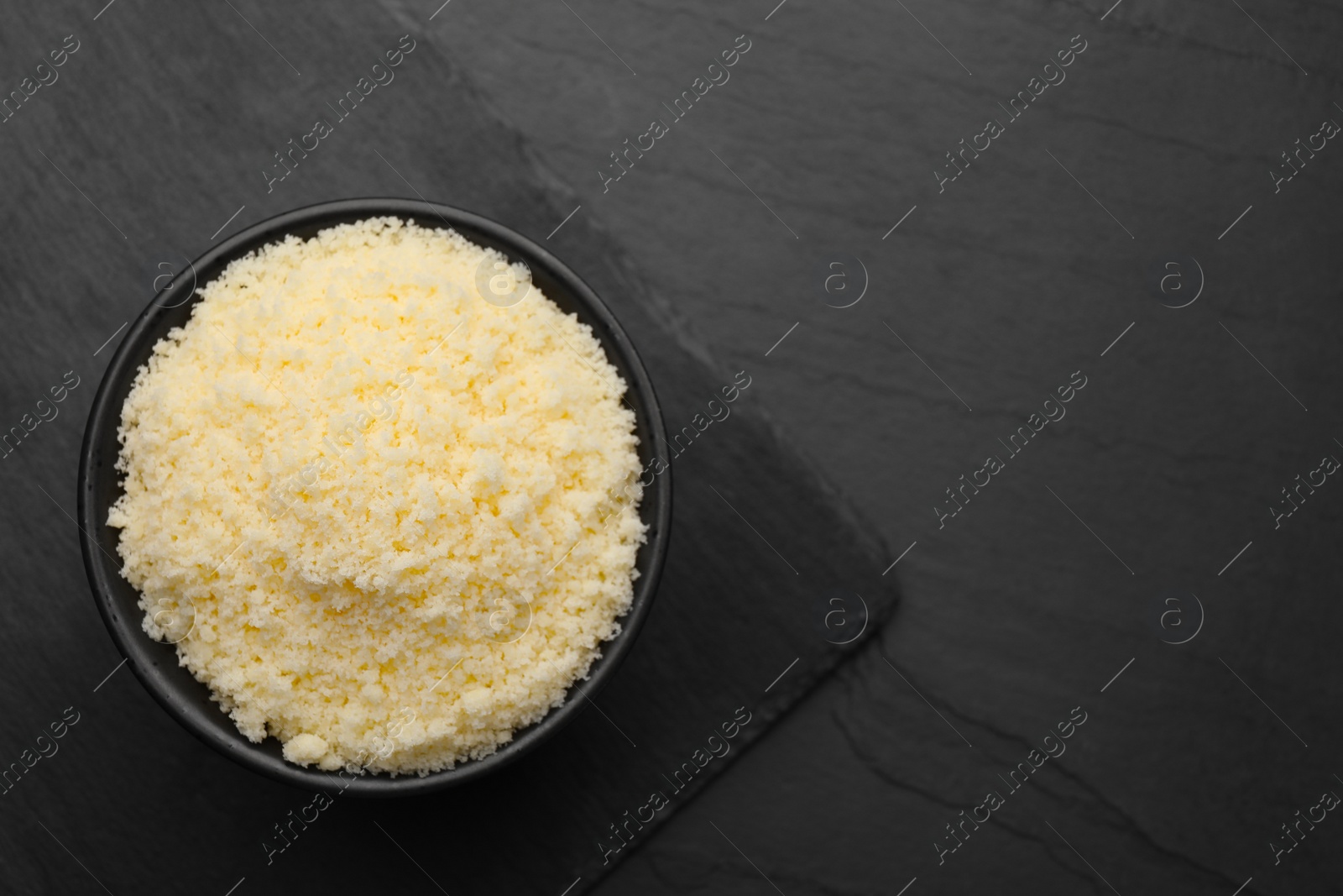 Photo of Bowl with grated parmesan cheese on black table, top view. Space for text