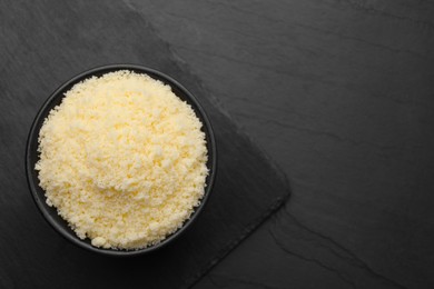 Photo of Bowl with grated parmesan cheese on black table, top view. Space for text