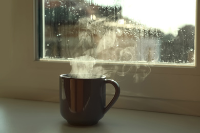 Cup of hot drink near window on rainy day. Space for text