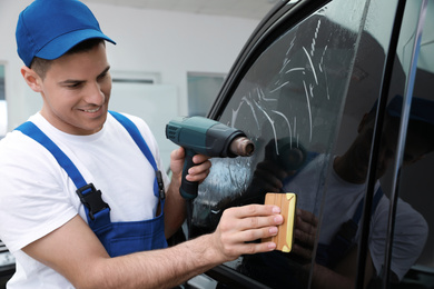 Worker tinting car window with foil in workshop