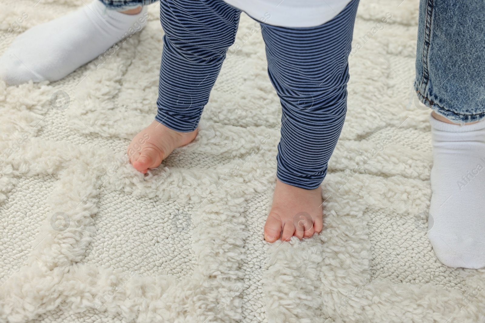 Photo of Mother supporting her son while he learning to walk on carpet, closeup