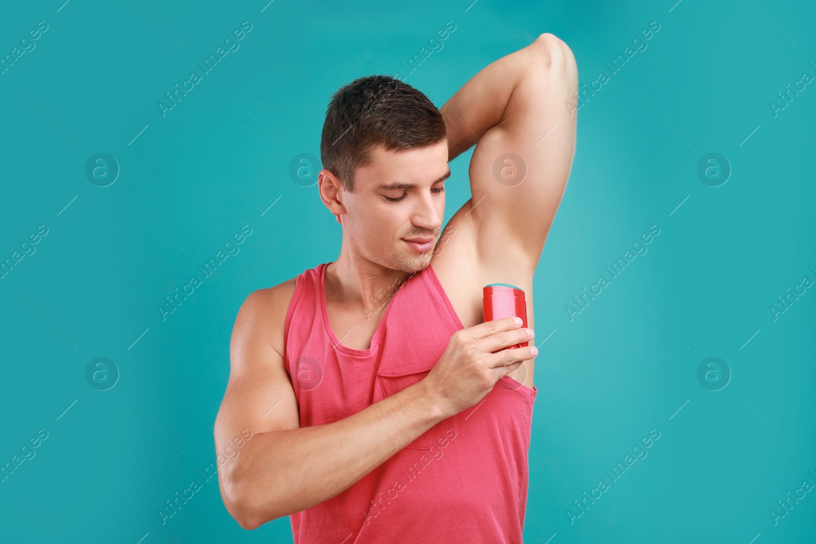 Photo of Young man applying deodorant to armpit on light blue background