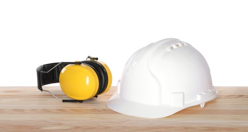 Photo of Hard hat and earmuffs on wooden table against white background. Safety equipment