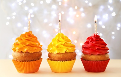 Photo of Delicious birthday cupcakes with candles on table against blurred background