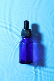 Photo of Bottle of face serum in water on light blue background, top view