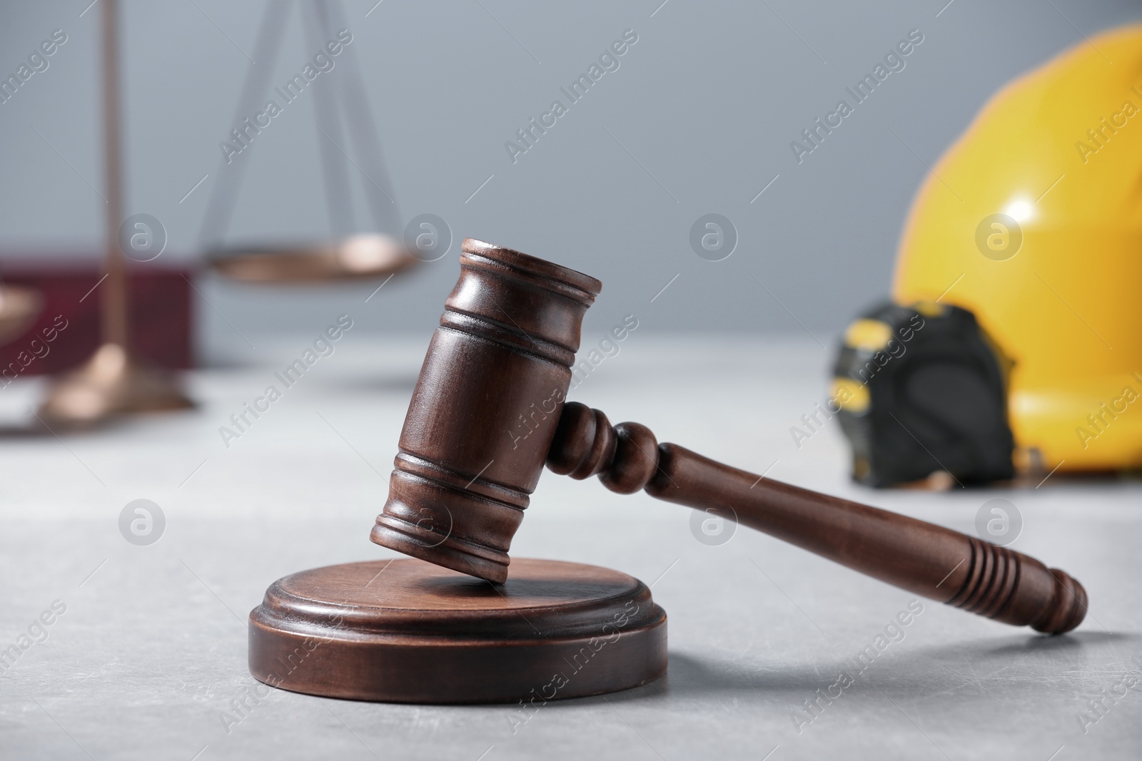 Photo of Construction and land law concepts. Judge gavel, scales of justice, tape measure with hardhat on light grey table