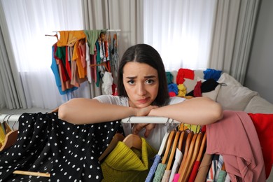 Photo of Pensive young woman with lots of clothes in room. Fast fashion