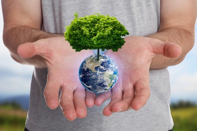 Image of Make Earth green. Man holding globe with tree on top outdoors, closeup