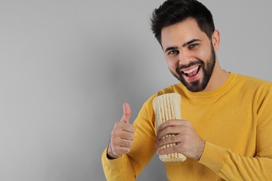 Photo of Happy young man with tasty shawarma showing thumb up on grey background. Space for text