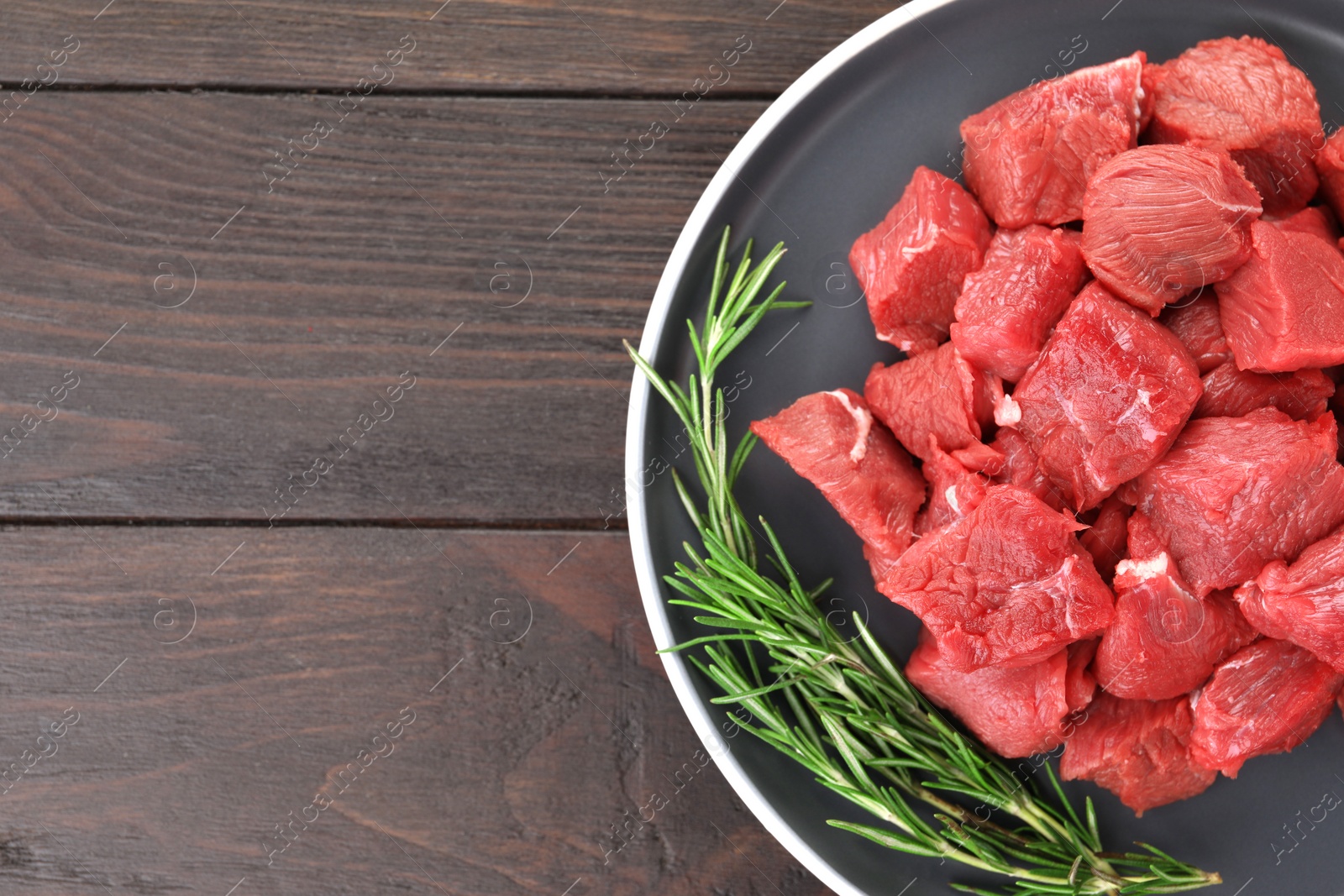 Photo of Pieces of raw beef meat with rosemary on wooden table, top view. Space for text