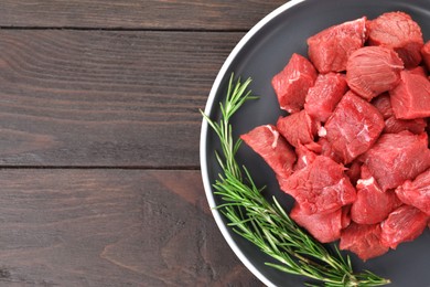 Photo of Pieces of raw beef meat with rosemary on wooden table, top view. Space for text