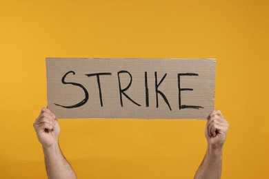 Photo of Man holding cardboard banner with word Strike on orange background, closeup
