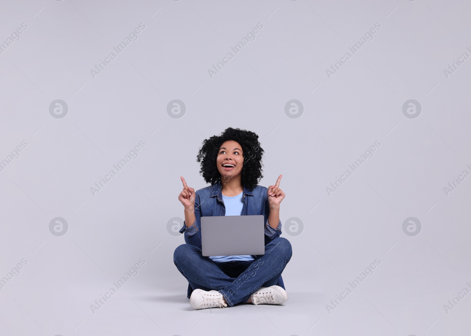 Photo of Happy young woman with laptop pointing at something on light grey background