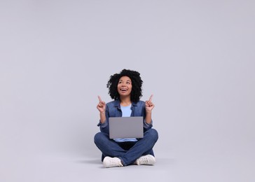 Happy young woman with laptop pointing at something on light grey background