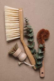 Cleaning brushes and eucalyptus leaves on pale brown background, flat lay