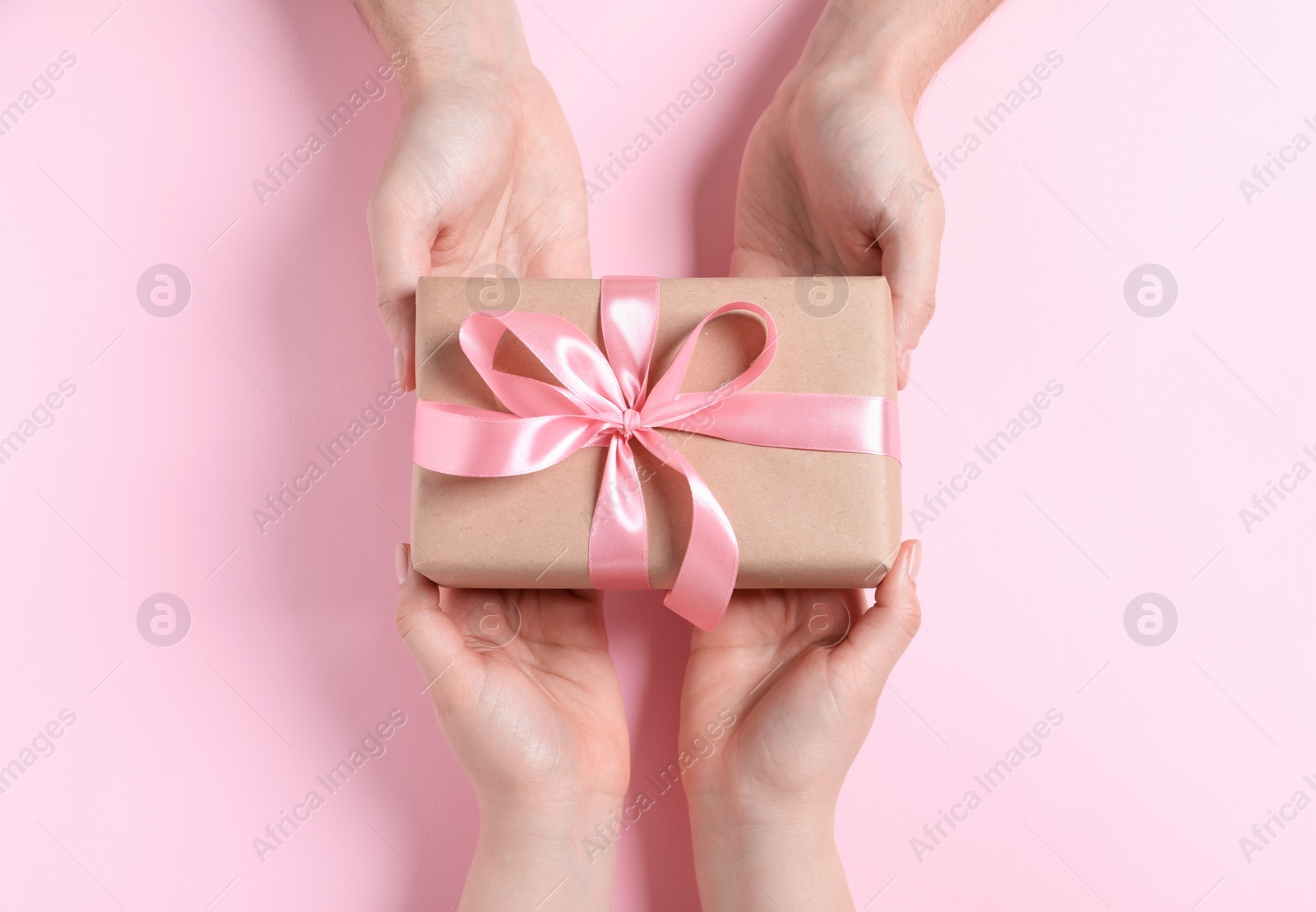 Photo of Man giving gift box to woman on pink background, top view