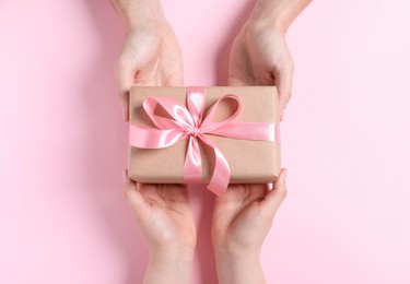 Photo of Man giving gift box to woman on pink background, top view