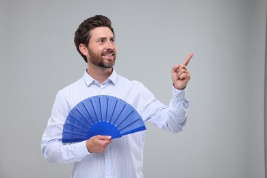 Happy man holding hand fan on light grey background