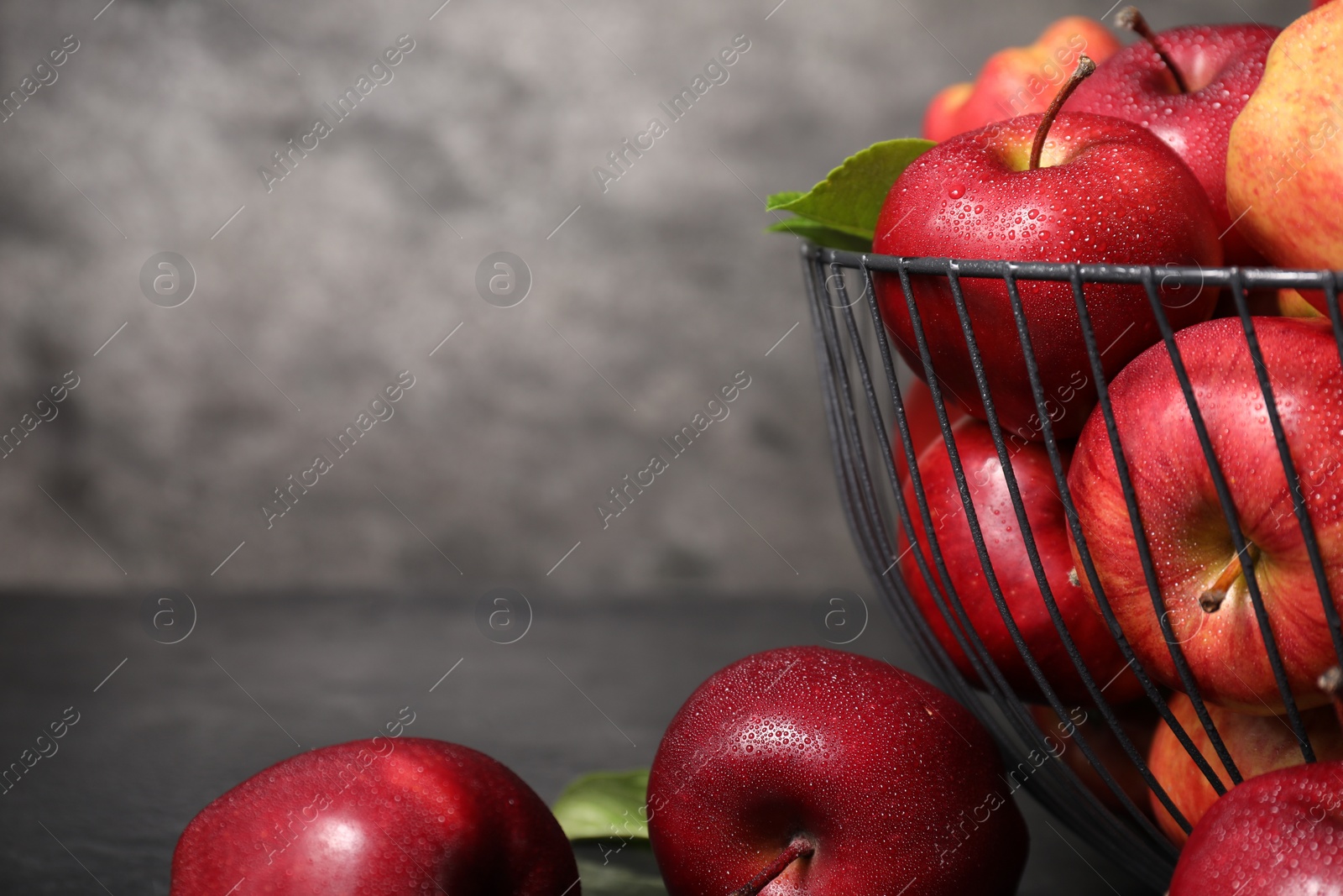 Photo of Fresh ripe red apples with water drops in metal bowl on table, closeup. Space for text