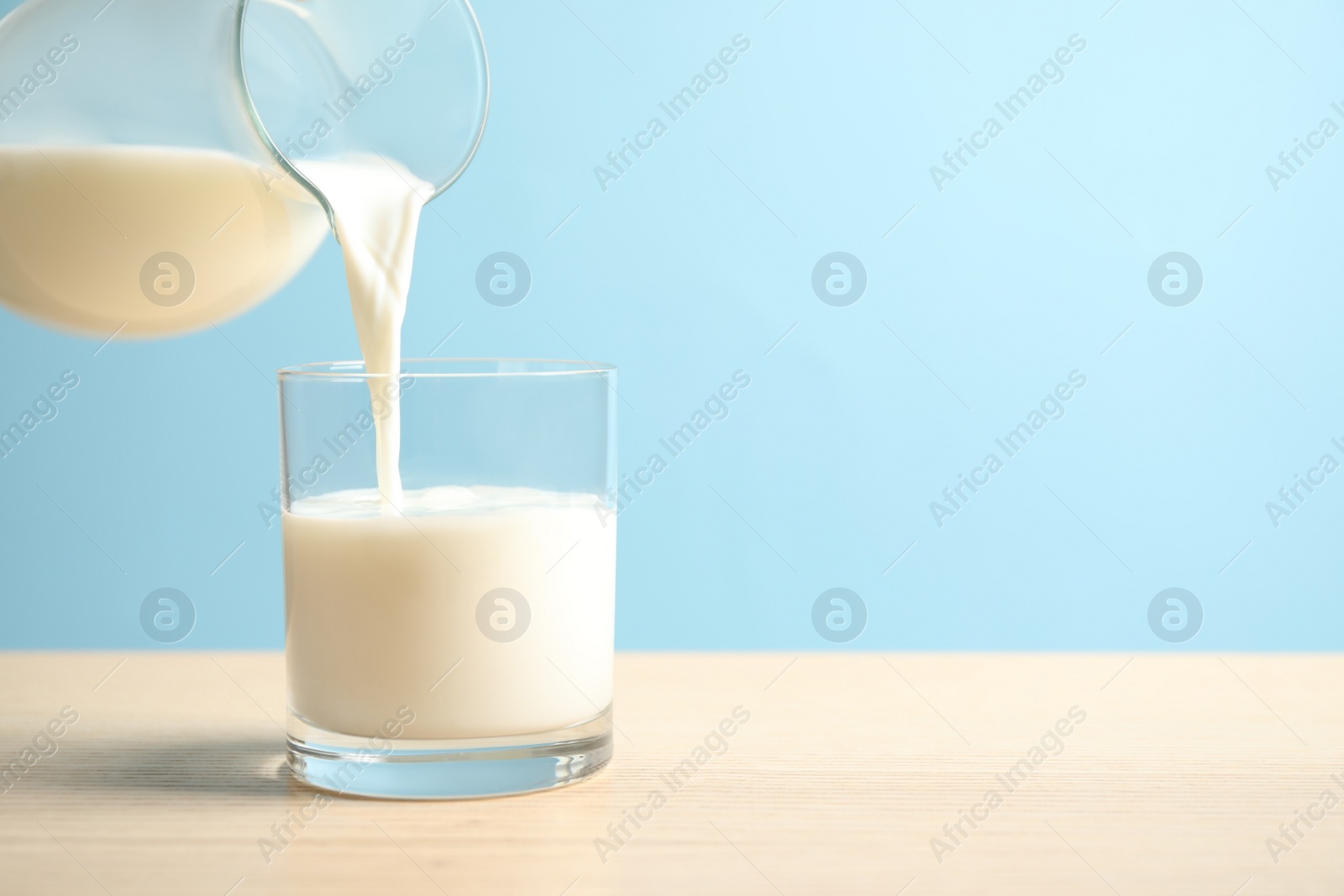 Photo of Pouring milk into glass on wooden table against light blue background. Space for text