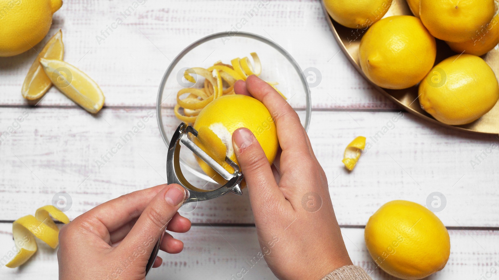 Photo of Man peeling lemon at white wooden table, top view