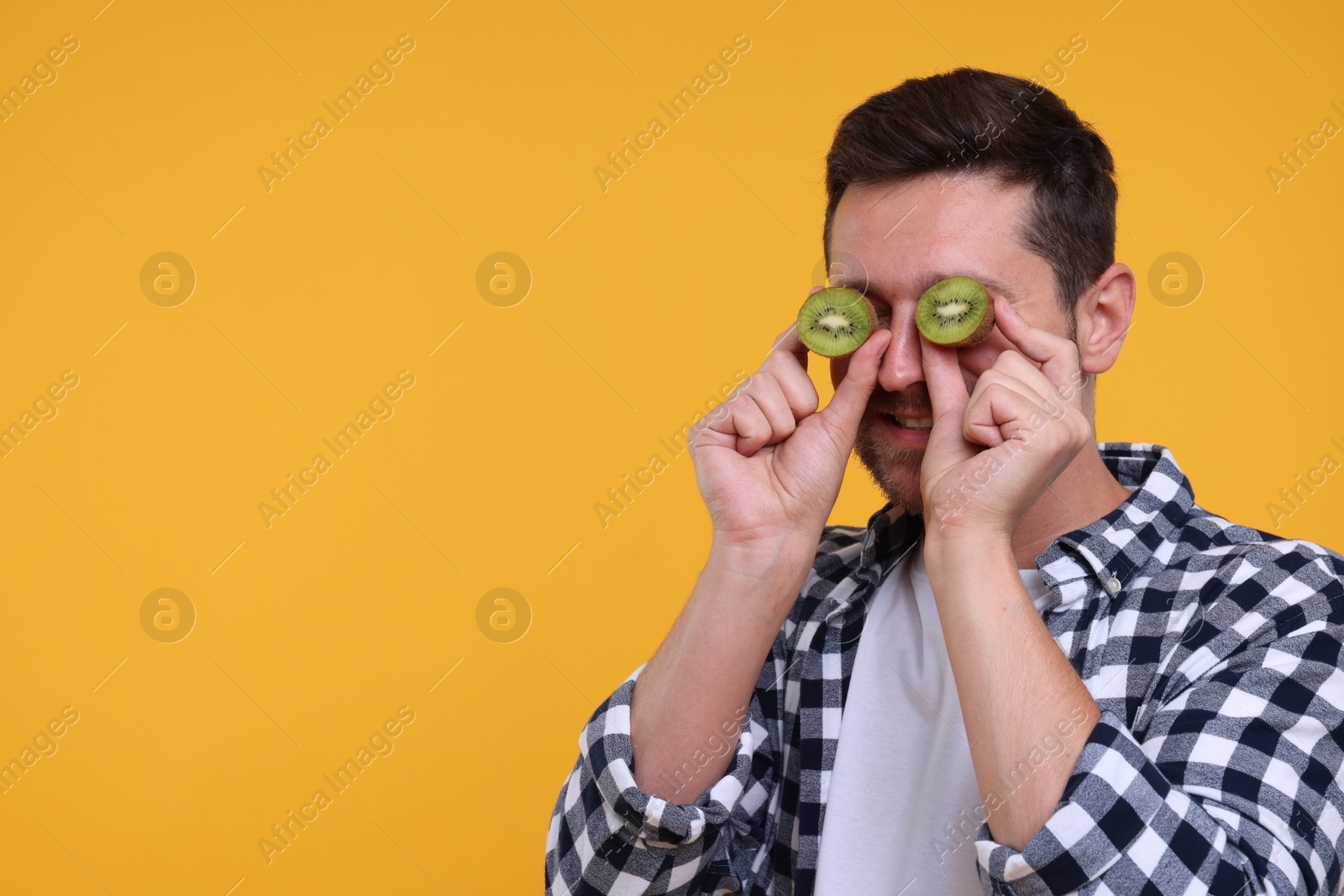 Photo of Man covering his eyes with halves of kiwi on yellow background. Space for text