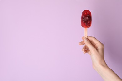 Photo of Woman holding delicious ice pop on light purple background, closeup view with space for text. Fruit popsicle