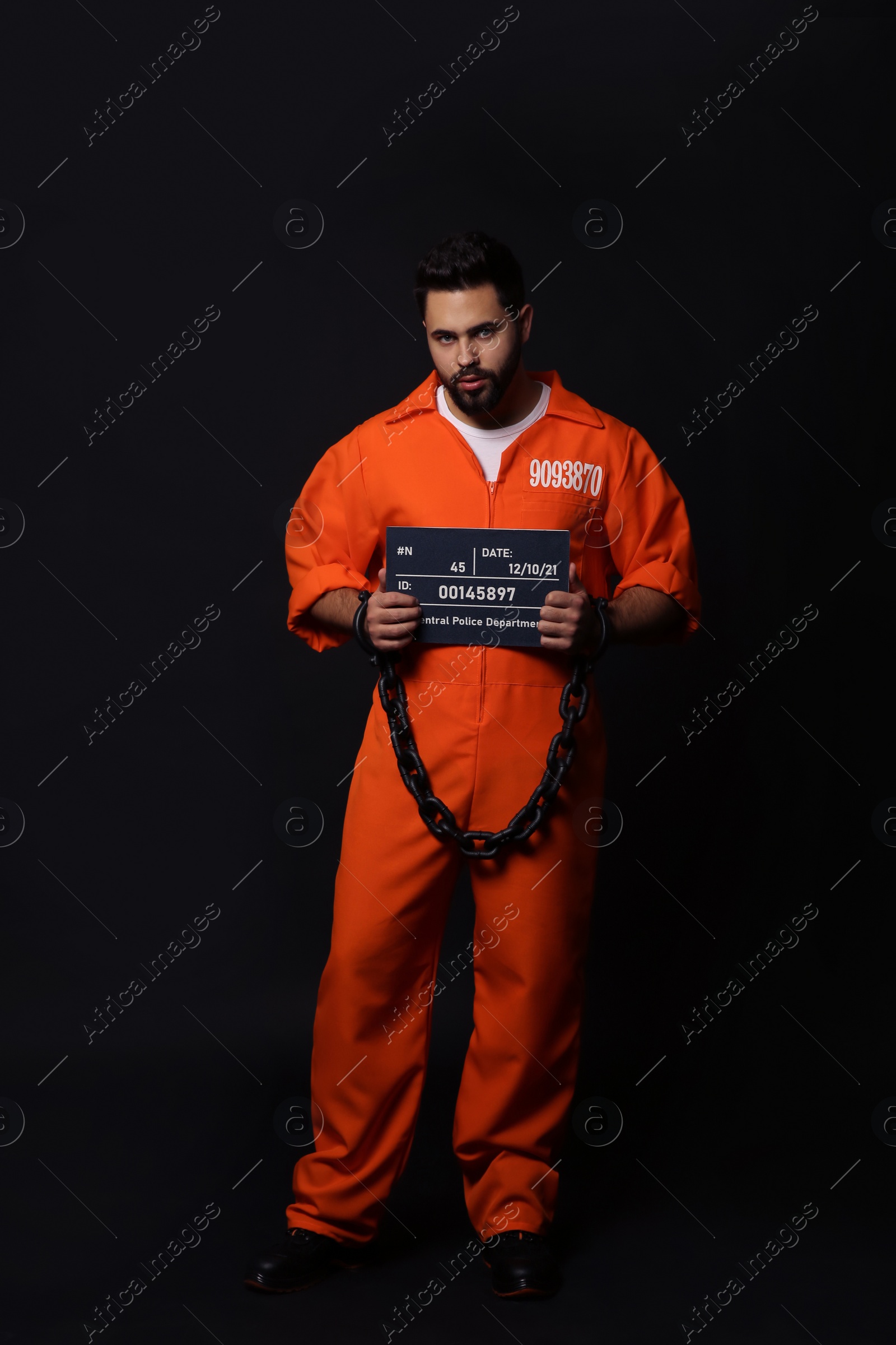 Photo of Prisoner with chained hands holding mugshot letter board on black background