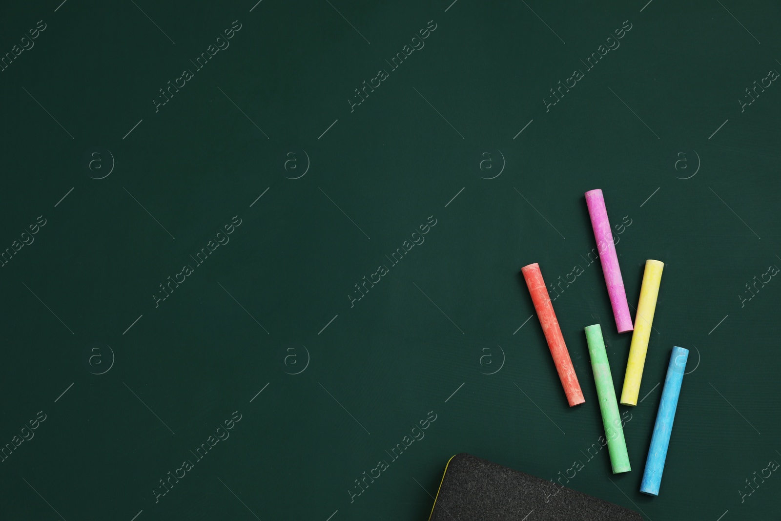 Photo of Colorful chalks and duster on green board, flat lay. Space for text