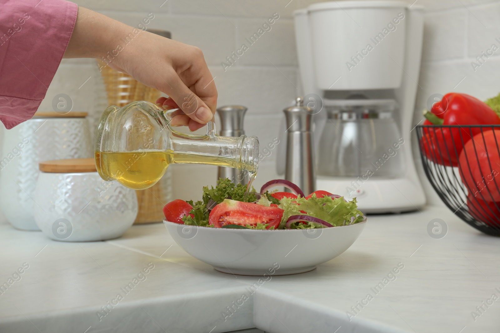 Photo of Woman pouring oil from jug into bowl with salad in kitchen, closeup