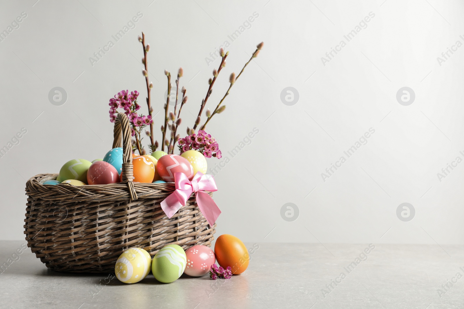 Photo of Wicker basket with painted Easter eggs and flowers on table, space for text