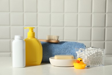 Baby cosmetic products, bath duck, cotton swabs and towel on white table against tiled wall. Space for text