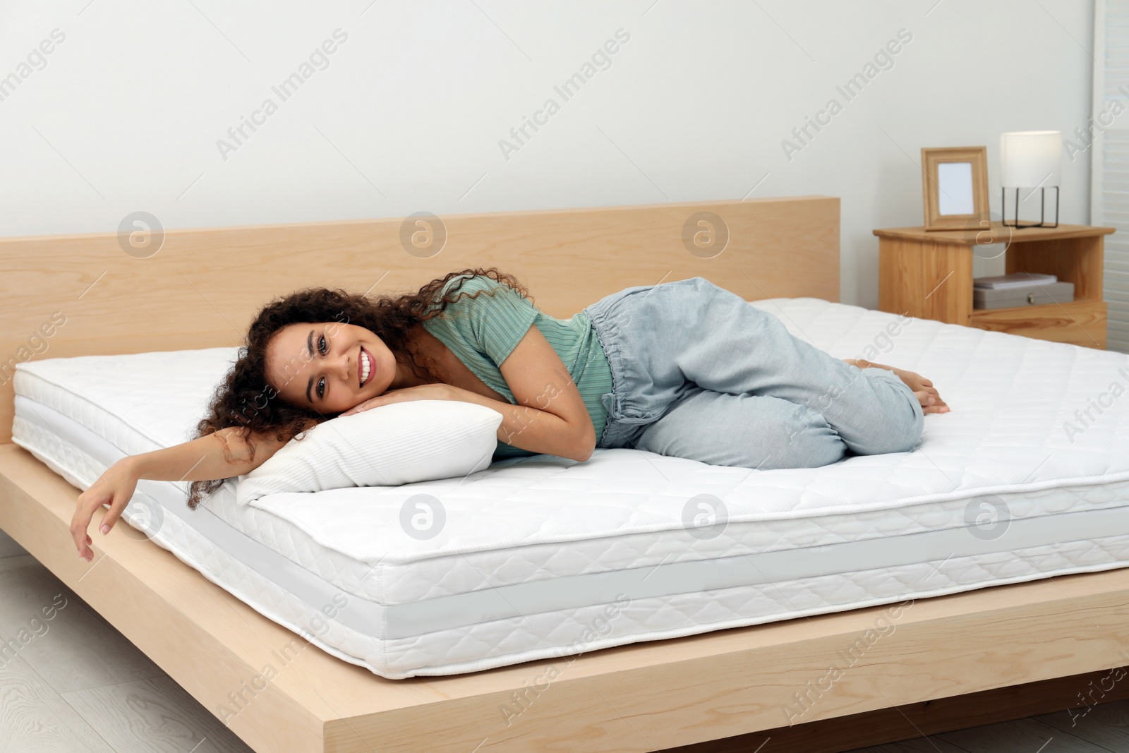 Photo of Happy young African American woman on bed with comfortable mattress and pillow at home