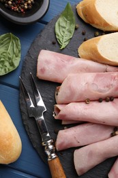 Rolled slices of delicious ham and baguette served on blue wooden table, flat lay