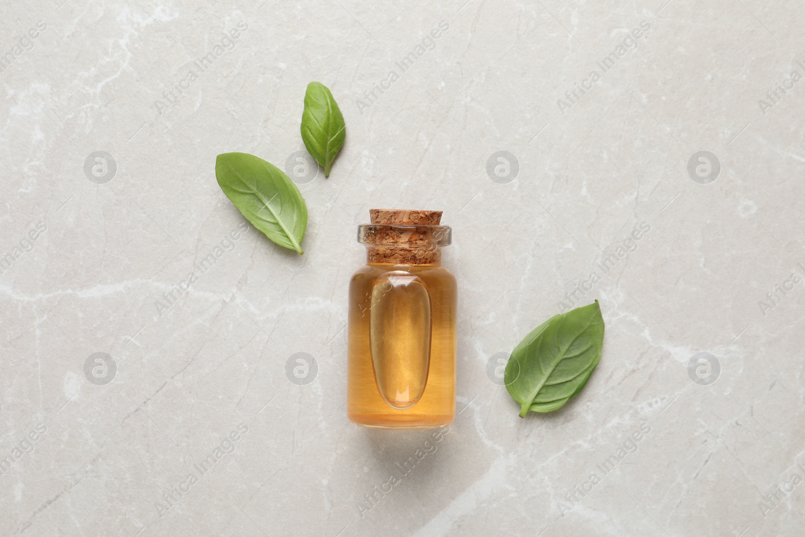 Photo of Bottle of essential basil oil and fresh leaves on light marble table, flat lay