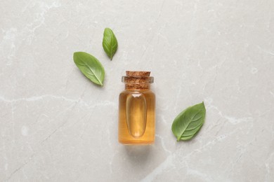 Photo of Bottle of essential basil oil and fresh leaves on light marble table, flat lay