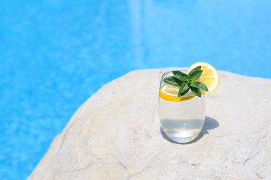 Photo of Refreshing water with lemon and mint on rock near swimming pool outdoors, space for text