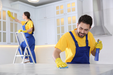 Photo of Professional young janitor cleaning table in kitchen