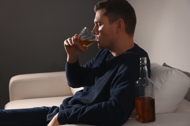 Photo of Addicted man drinking alcohol on sofa indoors